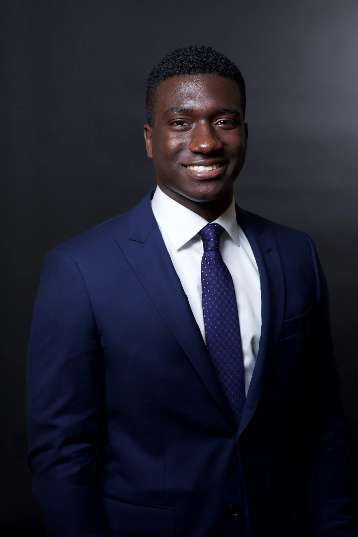 Corporate headshot of a young man in a navy suit and tie