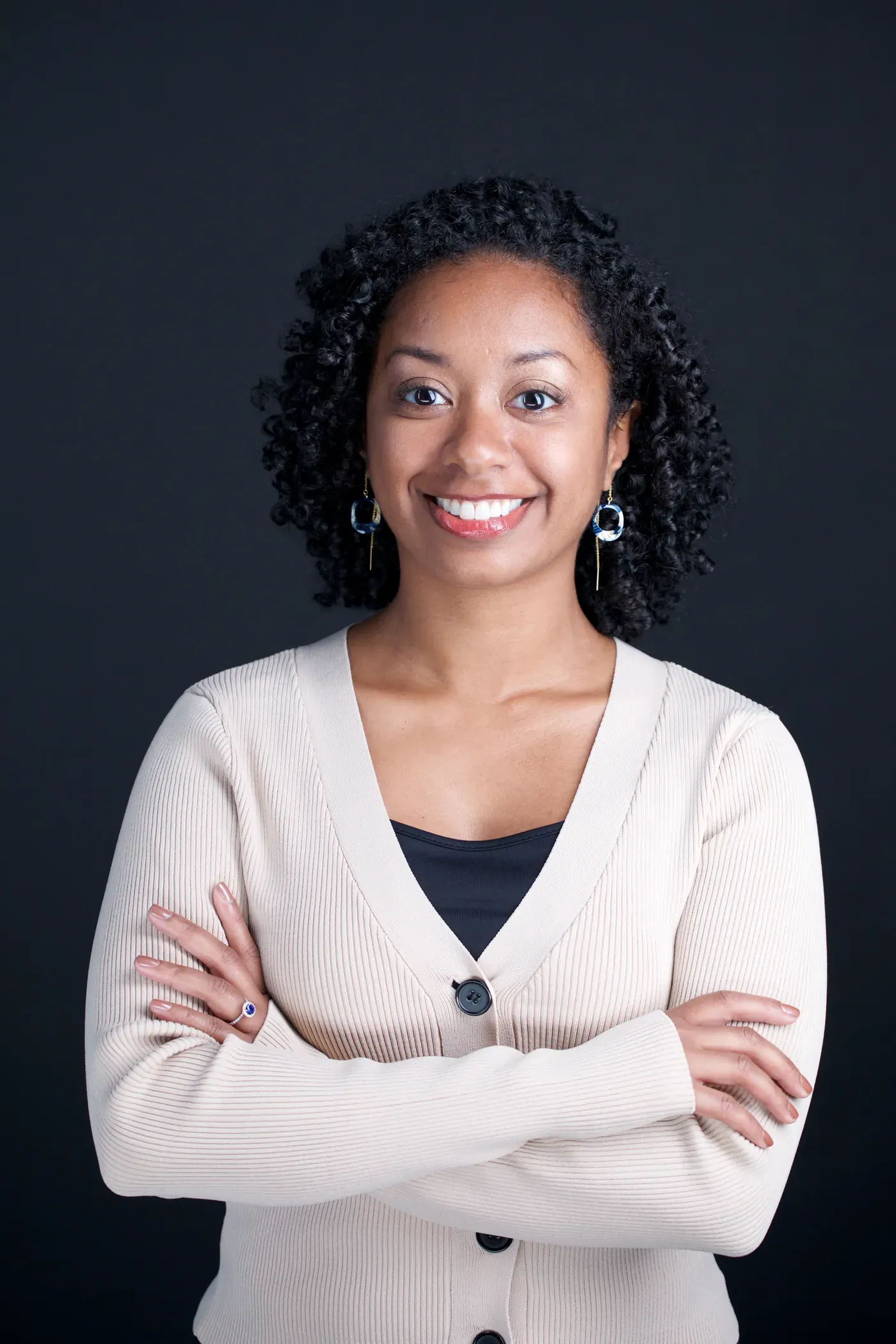 Smiling professional headshot of a woman with curly hair in a cream cardigan
