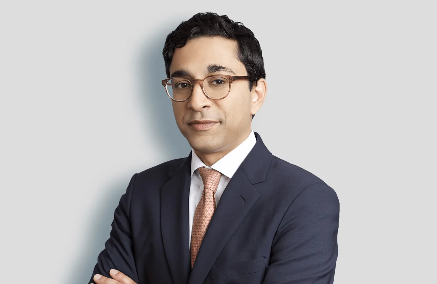 Team headshot of a man in glasses and a navy suit on a light gray backdrop